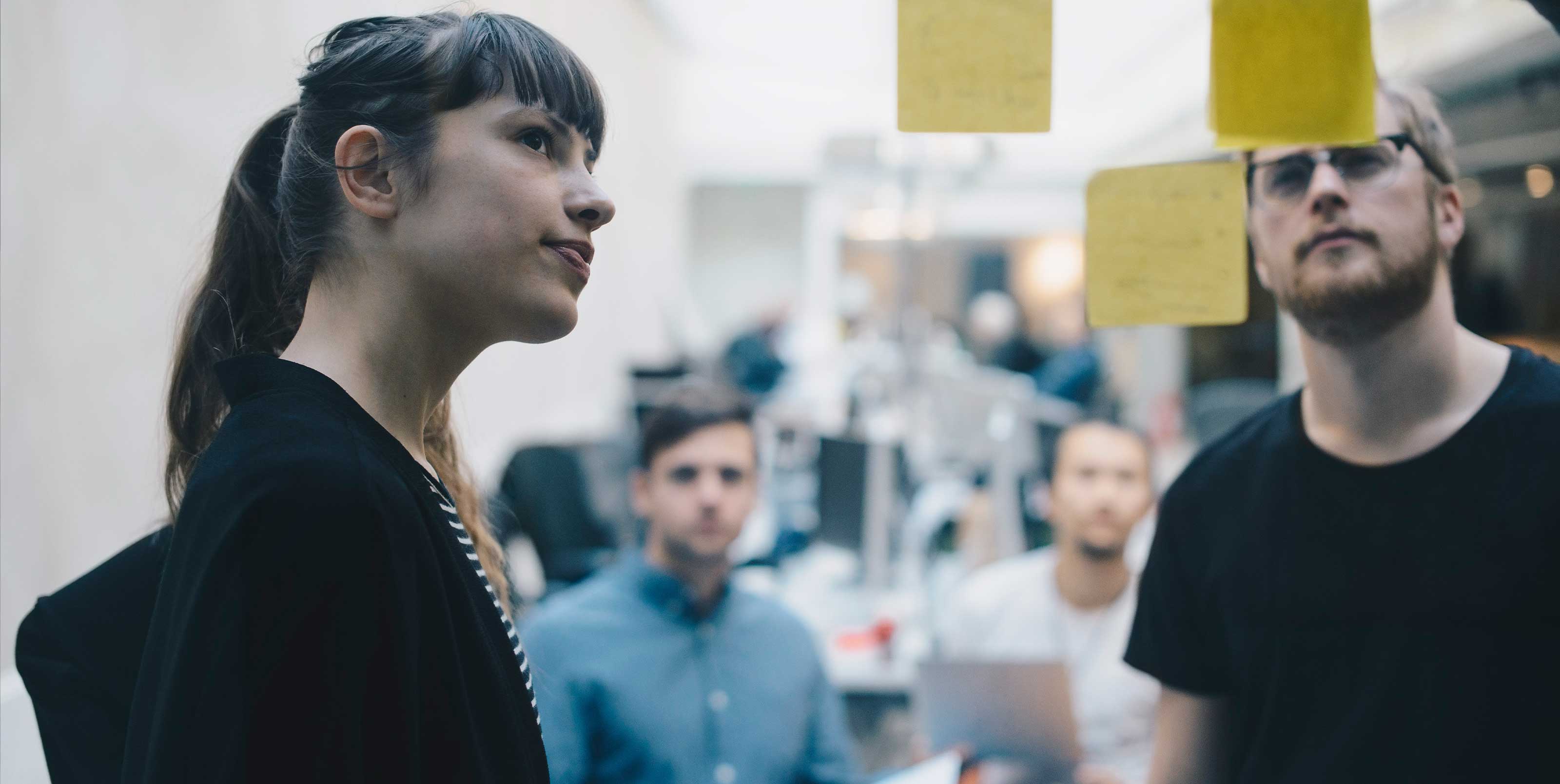 Four people look at yellow sticky notes on a wall in a workshop Four people look at yellow sticky notes on a wall in a workshop