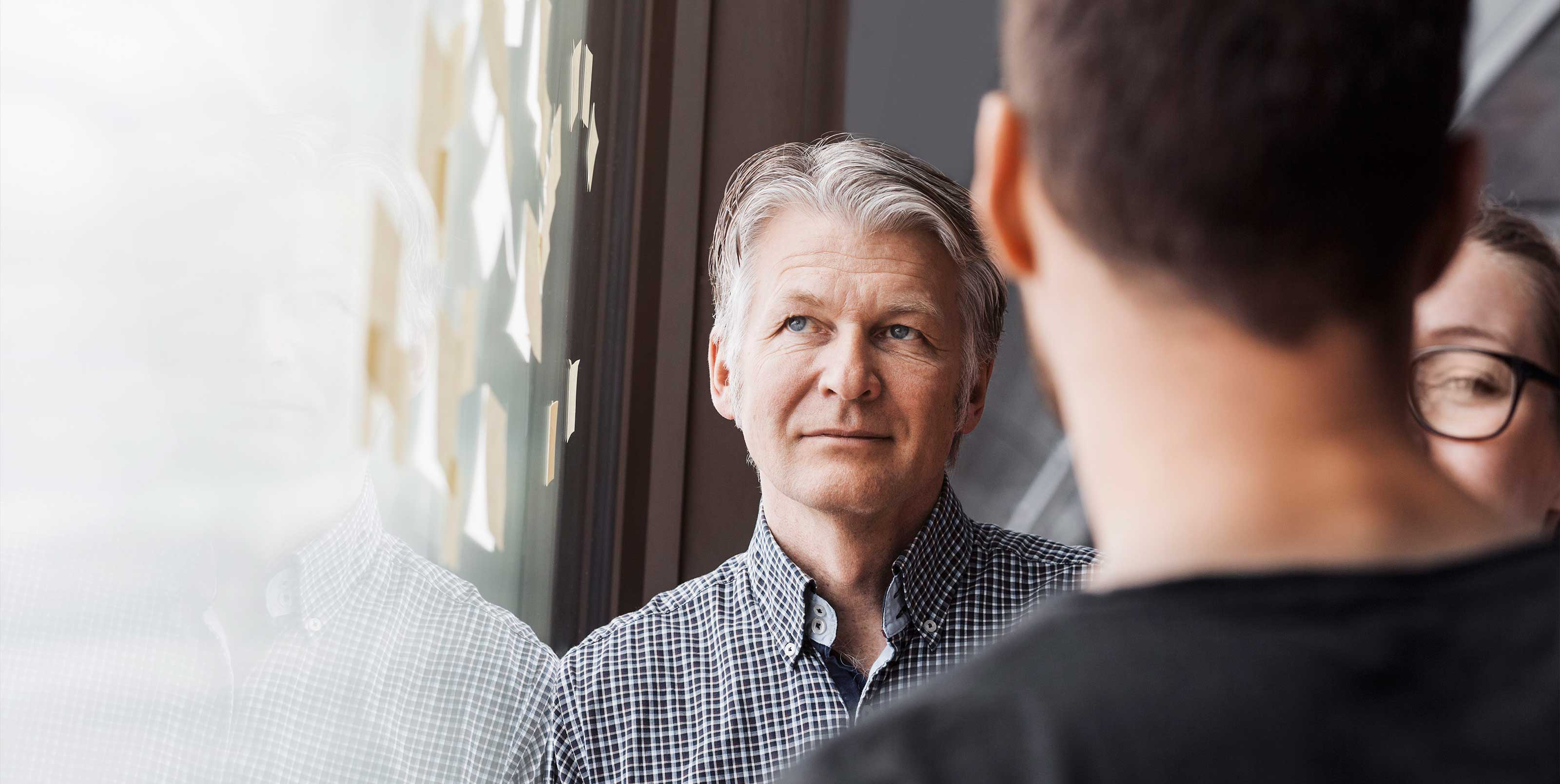 Man with thoughtful look in workshop with two other people Man with thoughtful look in workshop with two other people