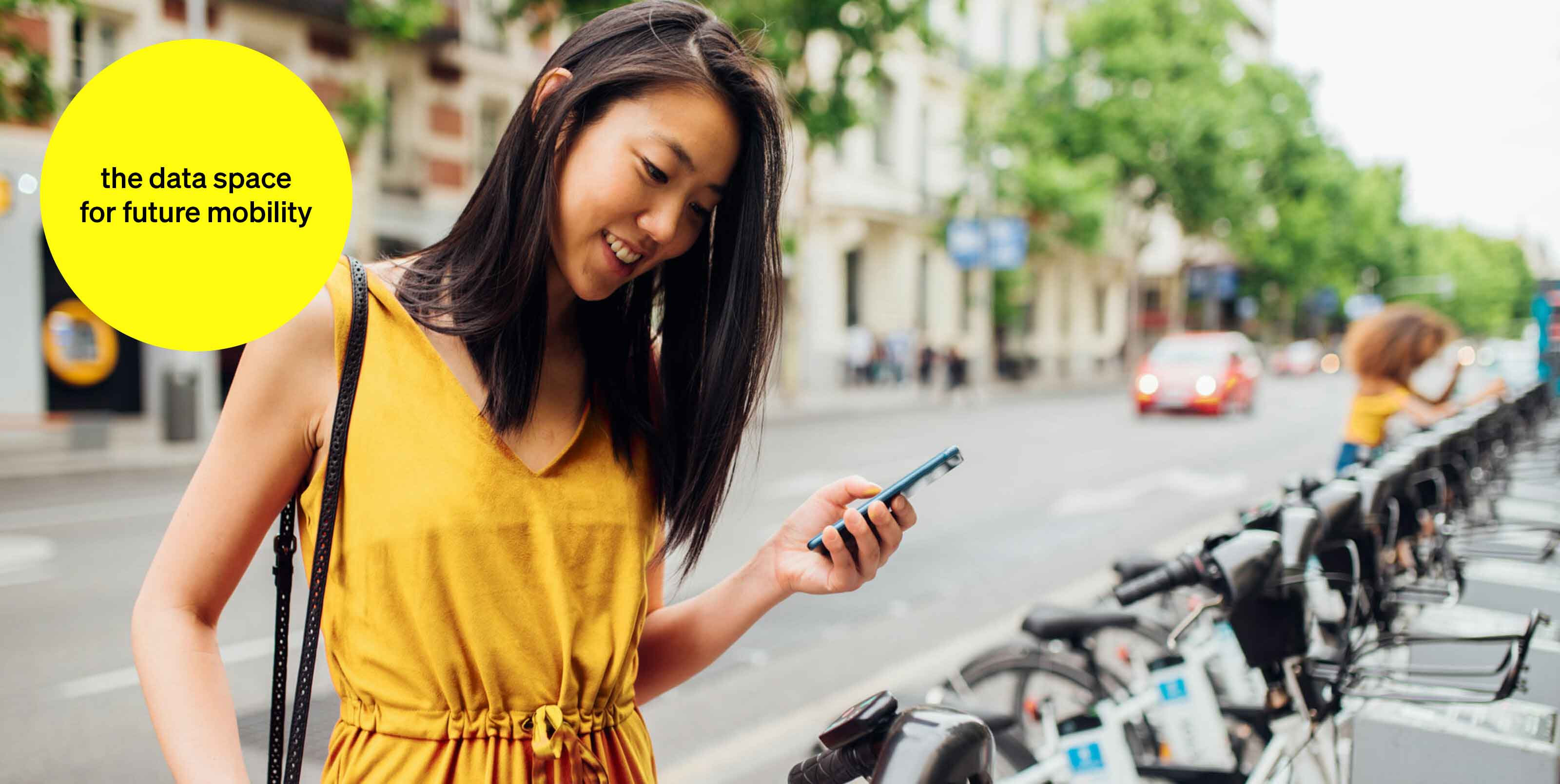 Woman with cell phone in hand at a bikesharing station - text module in round tile: data room for tomorrow's mobility Woman with cell phone in hand at a bikesharing station - text module in round tile: data room for tomorrow's mobility