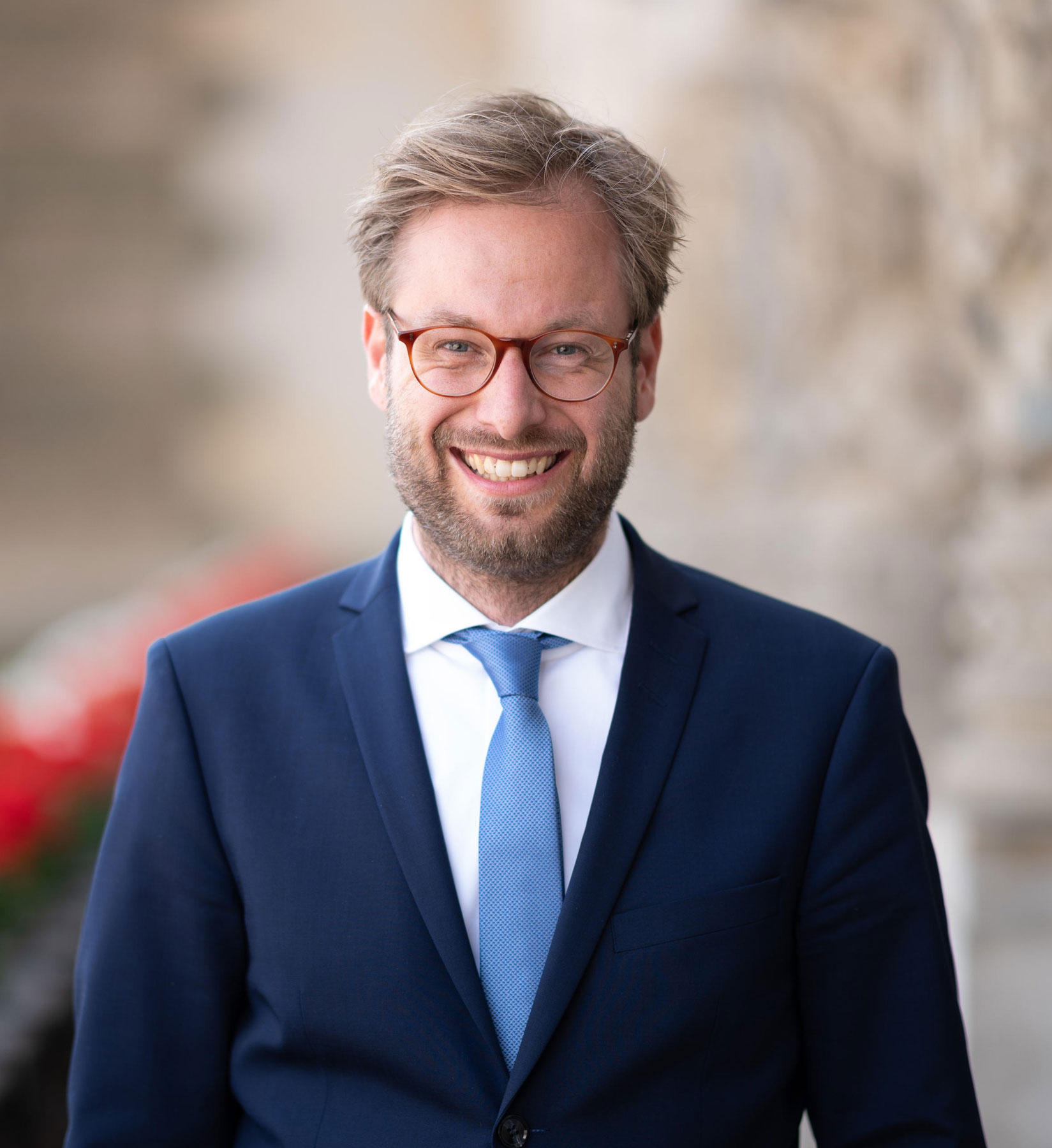 A smiling, bespectacled man in a blue suit and white shirt. A smiling, bespectacled man in a blue suit and white shirt.