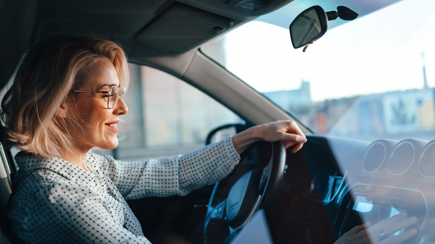 Woman sitting smiling in the driver's seat of a car with her left hand on the steering wheel. Shot from the perspective of the passenger. Woman sitting smiling in the driver's seat of a car with her left hand on the steering wheel. Shot from the perspective of the passenger.